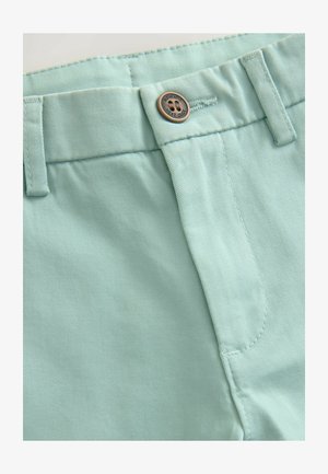 Lysgrønne bomuldsbukser med metalknaplukning, bæltestropper og glat tekstur. Sømmen har synlige syninger.