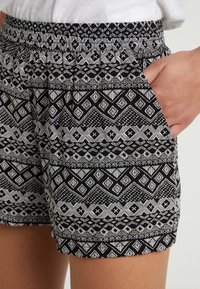 Černobílé šortky se vzorem s geometrickými designy, elastickým pasem a bočními kapsami. Textura vypadá měkce a lehce.