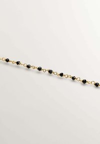 Pulsera en tono dorado con cuentas negras facetadas espaciadas de manera uniforme a lo largo de una cadena delicada, combinando brillo y textura en un diseño lineal.
