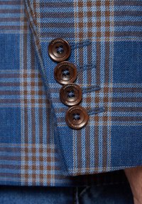 Niebiesko-brązowy marynarski mankiet w kratę z czterema ciemnobrązowymi guzikami, z jasnoniebieskim przeszyciem na teksturowanym materiale.