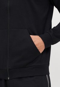 Zwarte zip-up hoodie van een soepele katoenmix, met zijzakken en ribgebreide manchetten. Strak ontwerp en getailleerde pasvorm.
