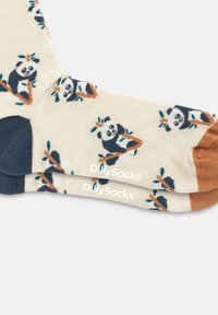 Calcetines con una base color crema, gráficos de pandas, hojas verdes y acentos azules. La zona de los dedos es de color azul oscuro, mientras que el talón es marrón.