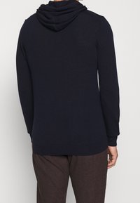 Marinblå huvtröja med avslappnad passform, tillverkad av mjukt material. Har en rundad nederkant, långa ärmar och en dubbellagrad huva.