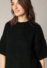 Pull en maille noire avec une coupe décontractée, des manches courtes et une surface texturée. L'encolure est ronde et côtelée. Tissu doux et confortable.