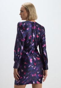 Abito con stampa floreale in tonalità di viola e rosa, realizzato in tessuto satinato. Presenta maniche lunghe, design aderente e chiusura con cerniera sul retro.