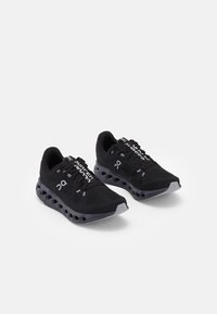 Schwarze Sportschuhe mit einem Obermaterial aus Netzgewebe, synthetischen Überzügen und einer gepolsterten Sohle mit sichtbaren Segmenten. Reflektierende Akzente an den Schnürsenkeln.