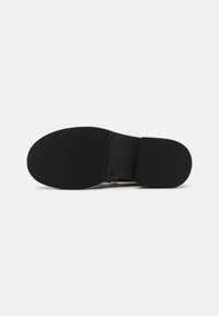 Suola di scarpa in gomma nera con un motivo testurizzato a righe. Presenta una sezione centrale liscia e un tacco arrotondato. Design leggero.