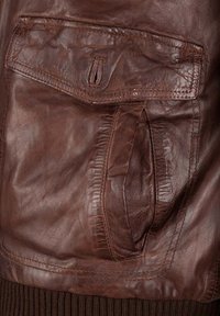 Braune Lederjacke mit einer seitlichen Tasche mit Klappe, strukturierter Oberfläche, geripptem braunem Stoff am unteren Ende und detaillierten Nähten.