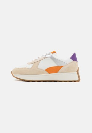 Zapatilla baja de ante beige, cuero blanco, detalles en naranja y púrpura, cordones blancos y una suela blanca gruesa con dibujo marrón.