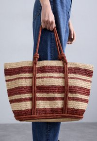 Torebka z tkanego słomy z czerwonymi i kremowymi paskami, z dwiema plecionymi uchwytami ze sznurka i naturalną teksturą. Lekko usztywniony kształt.