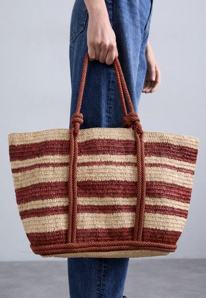 Woven tote torba od slame s crvenim i kremastim prugama, dva pletena uša od konopa i prirodnom teksturom. Lagano strukturirani oblik.