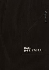 Sorte tekstureret stof med en lynlåslomme og trykt tekst "HALO 196819721981" i hvid. Vertikal ribbet design synlig.