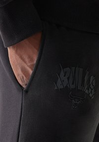 Μαύρο παντελόνι φόρμας με υφή, πλαϊνή τσέπη και μαύρο γραφικό λογότυπο με σχέδιο ταύρου στην περιοχή του μηρού.