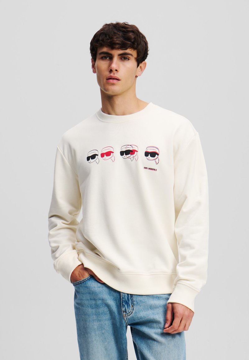 Crème sweatshirt met cartoongezichten met een zonnebril in zwart, rood en wit. Ronde hals, ribgebreide manchetten en tailleband, zachte textuur.