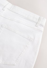Vue arrière d'un jean en denim blanc montrant des passants de ceinture, une taille et une seule poche arrière avec des coutures visibles.