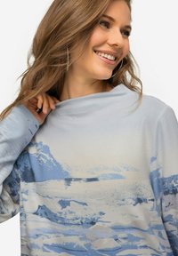 Chemise à manches longues bleu clair avec un imprimé de paysage montagneux dans des nuances de bleu et de blanc, avec une texture douce et lisse.