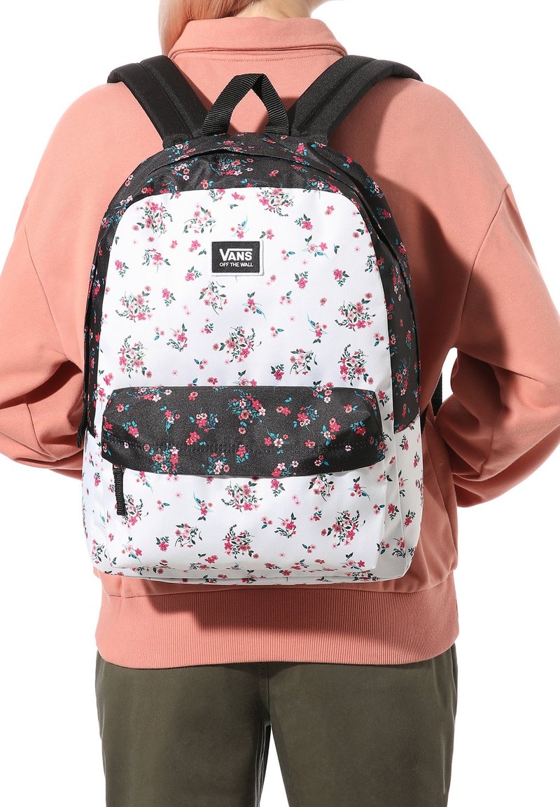 Zaino con motivo floreale, fondo bianco e dettagli neri, dotato di spalline regolabili e tasca frontale con zip. Il materiale appare resistente.