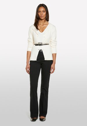 Blazer crème avec un col structuré et des boutons, cintré à la taille par une ceinture noire à clous. Associé à un pantalon noir ajusté et des ballerines.