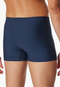 Pantaloni da bagno blu navy con righe verticali, caratterizzati da una vestibilità aderente e una cintura elastica. Texture liscia con cuciture piatte.