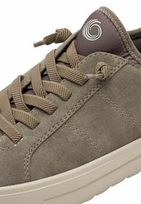 Braune Wildledersneaker mit hellbraunen Schnürsenkeln, strukturiertem Obermaterial, rundem Logo auf der Zunge und einer hellen Gummisohle.