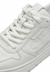 Sneakers bianchi con tomaia in pelle liscia, accenti testurizzati, lacci rotondi, perforazioni sulla punta e suola in gomma a contrasto.