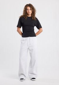 Musta istuva t-paita lyhyillä hihoilla ja poimuttamalla koristeltu, yhdistetty löysiin, vaaleanharmaisiin collegehousuihin ja mustilla yksityiskohdilla varustettuihin valkoisiin lenkkikenkiin.