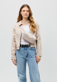 Borsa a tracolla in beige e crema, forma rettangolare, materiale texturizzato, dotata di una sottile tracolla regolabile e una patch con logo sulla parte anteriore.