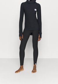 Top nero a maniche lunghe con colletto alto e patch con logo. Leggings neri con design aderente, entrambi realizzati in materiale elastico e liscio.
