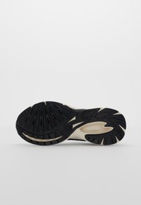 Semelle de chaussure de course noire avec des motifs de sculpture texturés et une semelle intermédiaire couleur crème. Forme arrondie avec des rainures proéminentes pour l'adhérence.
