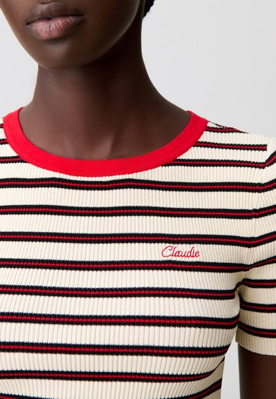 Top de manga corta de punto acanalado en color crema con rayas horizontales rojas y negras. Cuenta con un cuello rojo y la palabra "Claudie" bordada en rojo.