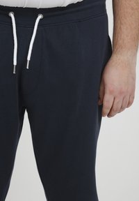 Marineblaue Baumwoll-Jogginghose mit elastischem Bund und weißen Kordeln. Mit einer Seitentasche und einer weichen, glatten Textur.