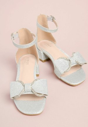 Hõbedased sädelevad pahkluu rihmaga sandaalid ruudukujulise varbaga, suure põimikuga ja rhinestone kaunistustega põimikul; tekstureeritud materjal ja plokk-konts.