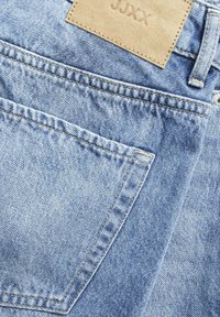 Lyseblå denimjeans med teksturert overflate, med et lærmerke merket "JUXX," synlige sømmer, og standard baklomme-design.