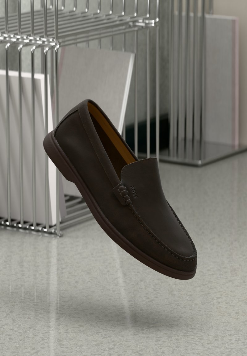 Chaussures en cuir marron à enfiler avec une texture lisse, bout arrondi, détails de couture subtils et une semelle en caoutchouc durable reposant sur une surface réfléchissante.