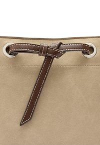 Beżowa zamszowa torba z brązowym skórzanym sznurkiem, przewleczonym przez srebrne oczka, z wyróżniającym się kontrastowym przeszyciem.