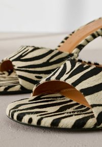 Chaussures à talons ouvert, avec un motif zèbre noir et crème, fabriquées en matériau texturé en fourrure, présentant une doublure intérieure lisse.