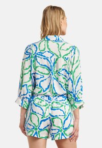 Bloemrijke korte set van witte stof met groene en blauwe organische patronen. Bevat een overdrapeerde blouse en shorts met elastische taille en zakken.