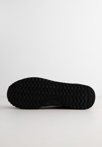 Black rubber shoe sole with a wavy tread pattern, circular indentation, and a slight lip at the heel. No visible branding or decorative elements.