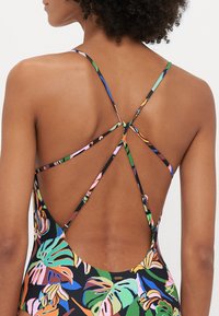Multicolored swimsuit featuring a tropical leaf design, with a crisscross back strap detail and a low cut back. Made from smooth, stretchy material.