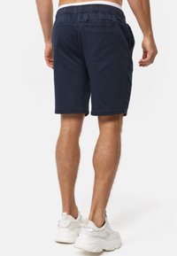 Shorts bleu marine avec une ceinture élastique, une coupe ajustée, des poches latérales et une poche arrière. Confectionnés dans un tissu doux et léger.