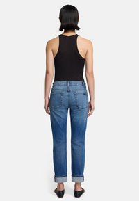 Czarny top na ramiączkach, niebieskie dżinsy z prostymi nogawkami, z podwiniętymi nogawkami i tylnymi kieszeniami. Gładka tekstura i średni odcień kolorystyczny.