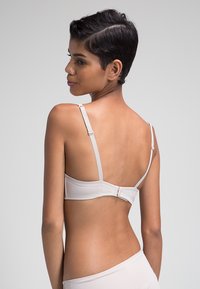 Sostén color beige claro con tirantes ajustables, tejido suave y cierre de gancho y ojal en la parte posterior. Diseño sencillo, sin patrones o acentos adicionales.