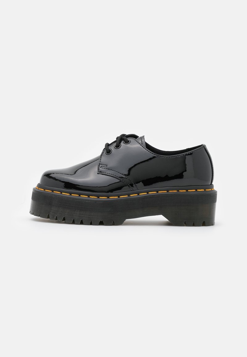 Scarpa di vernice nera con punta tonda, suola in gomma testurizzata spessa, cuciture gialle e design con lacci.