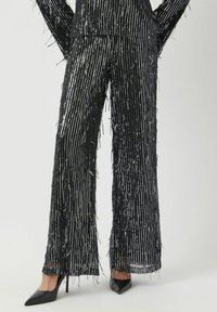 Zwarte wijde broek met metallic verticale strepen, voorzien van franjes langs de randen. Gecombineerd met zwarte puntige hakken.
