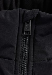 Primer plano de una chaqueta aislante negra, con un cierre central de cremallera con herrajes de plástico negro, textura acolchada y detalles de costura.