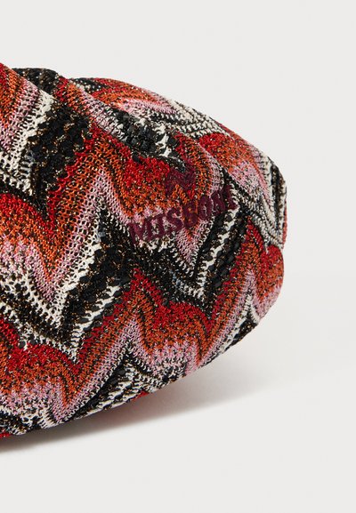 Flerfärgad stickad väska med ett zigzag-mönster i röd, svart, rosa och vit. Texturerad textil med dekorativa detaljer och logotyp.