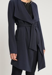 Cardigan enveloppant bleu marine en tissu doux et texturé. Manches longues, devant ouvert, taille nouée et poches latérales.