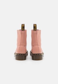 Botas de tobillo de cuero rosa con punta redondeada, suela gruesa marrón y costuras amarillas. La lengüeta trasera tiene una etiqueta marrón con texto amarillo.