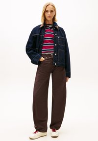 Chaqueta vaquera con cuello marrón, camiseta de rayas rojas y azul marino, pantalones marrones de pierna ancha y zapatillas blancas con cordones rojos.