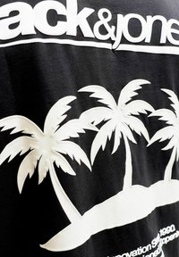 Μαύρο ύφασμα με λευκές ανάγλυφες φοίνικες και μερικό κείμενο "Jack & Jones" στην κορυφή, με τροπικό νησιωτικό σχέδιο.